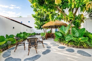 An outdoor seating area with a thatched-roof gazebo, surrounded by tropical plants and a stone pathway. - Opal Oasis (Gadhdhoo)