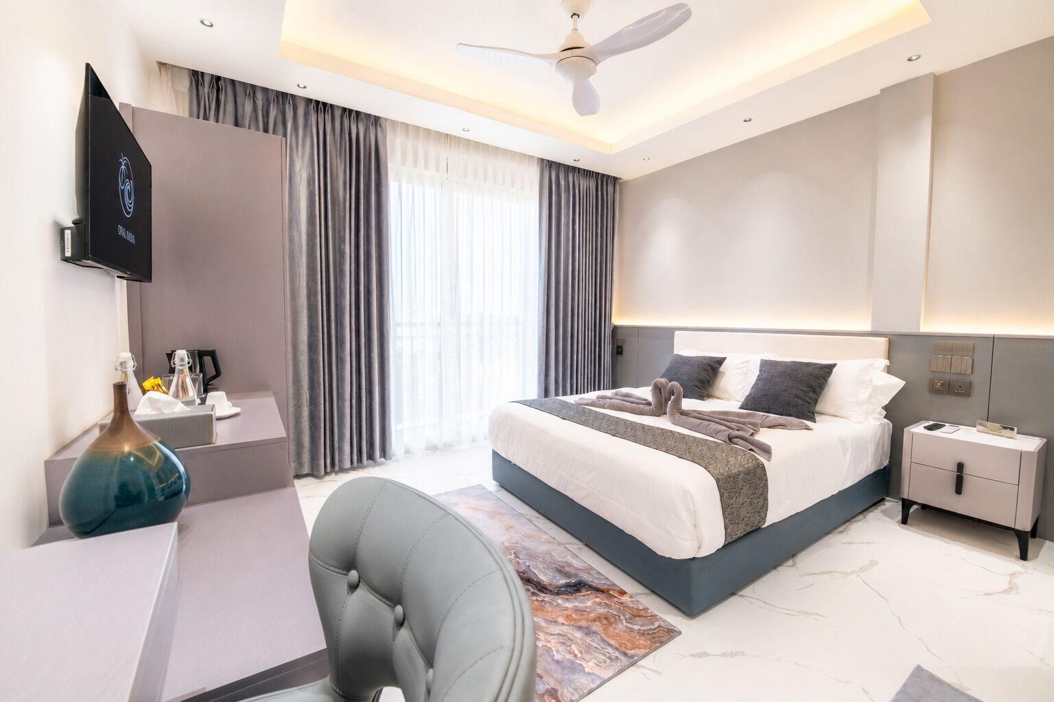 Una habitación de hotel moderna con una cama, mesita de noche, televisor y un escritorio con silla.