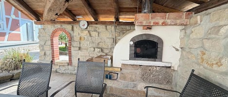 Un patio al aire libre con paredes de piedra, un horno de ladrillo, sillas de metal y una mesa de madera.