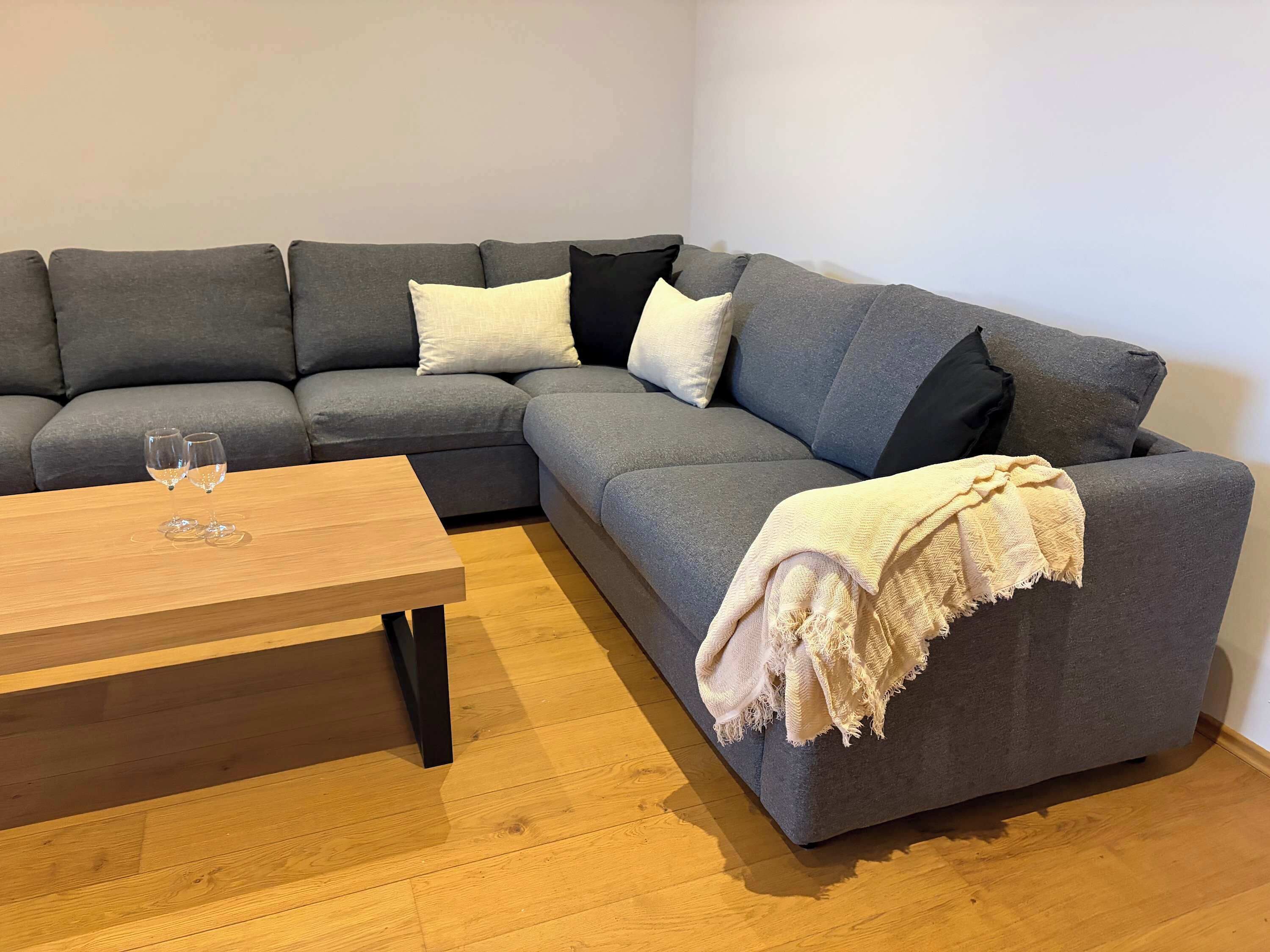 Een moderne woonkamer met een grijze modulaire bank, een houten salontafel en een beige plaid.