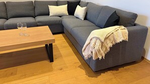 Ein modernes Wohnzimmer mit einem grauen Ecksofa, einem Holztisch und einer beigen Decke.