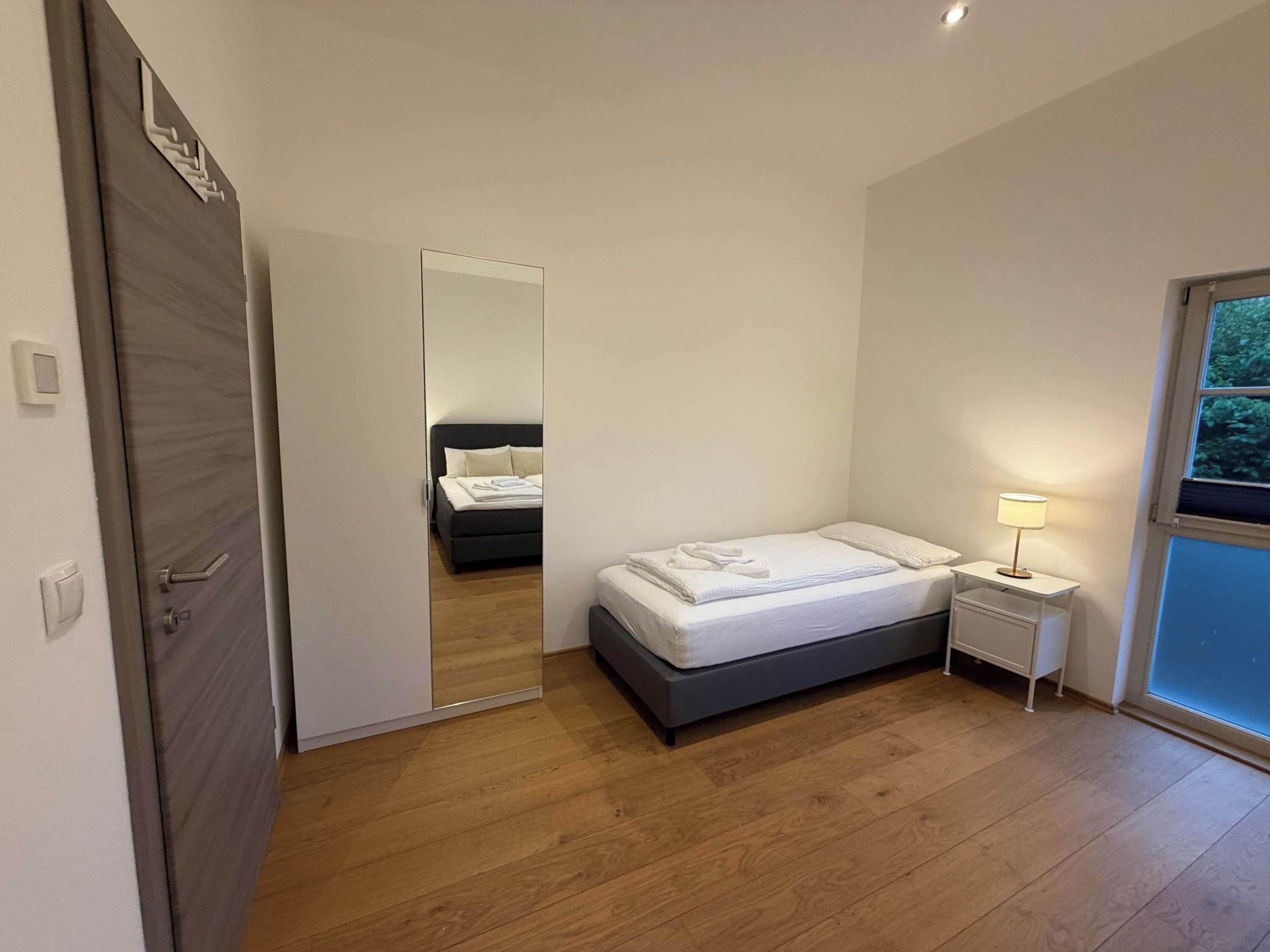 A bedroom with a bed, bedside table, and a mirror.