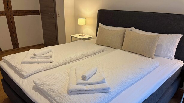 Ein Hotelzimmer mit einem großen Bett, zwei Kissen, einer Nachttischlampe und ordentlich gefalteten Handtüchern.