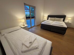 A bedroom with two beds, a large window, and bedside lamps.