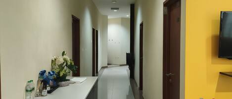 A hotel hallway with a reception desk, a fire extinguisher, and a television on the wall.