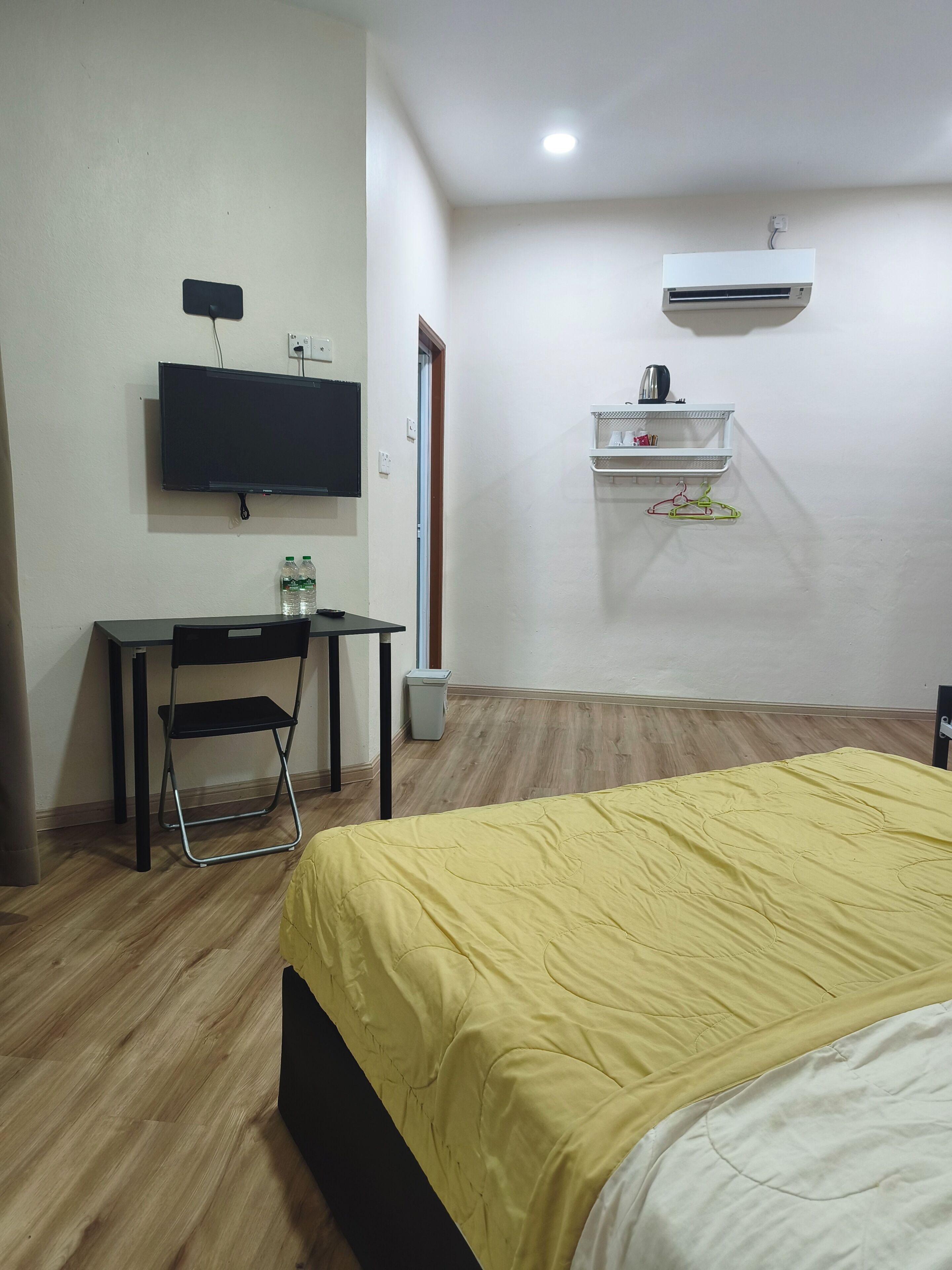 A room with a bed, a desk, a chair, a television, and a wall-mounted shelf.