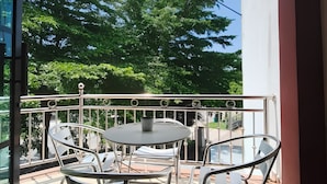 A balcony with a table and chairs, a flag, and a view of trees. - Tanjong Inn by StayZy (Kota Bharu)