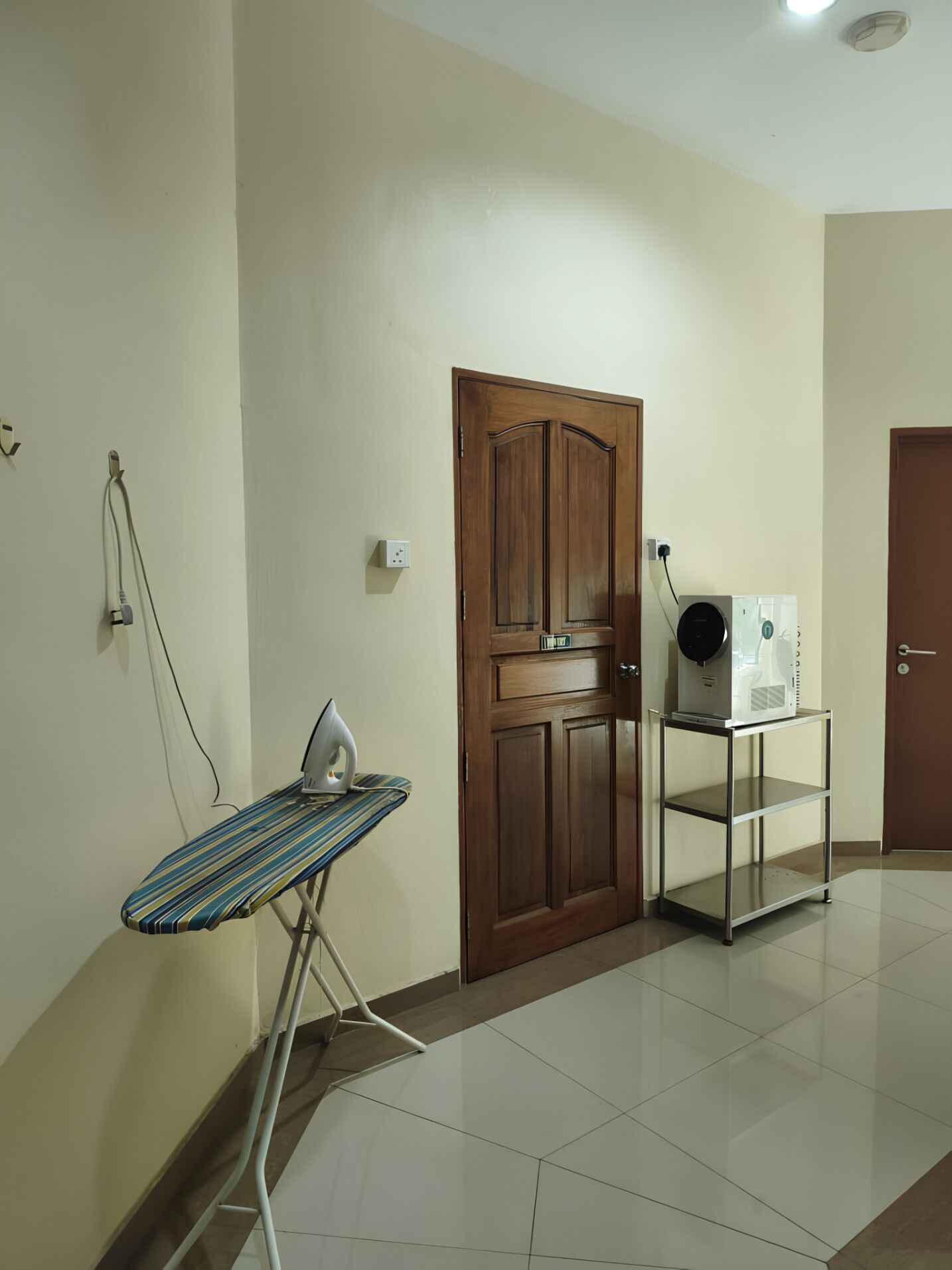 A room with a wooden door, an ironing board, and a small table with a device on it.