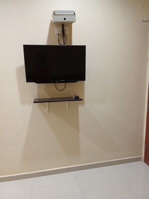 Un téléviseur fixé au mur, avec un meuble en dessous, une prise électrique au-dessus et une porte sur la droite.