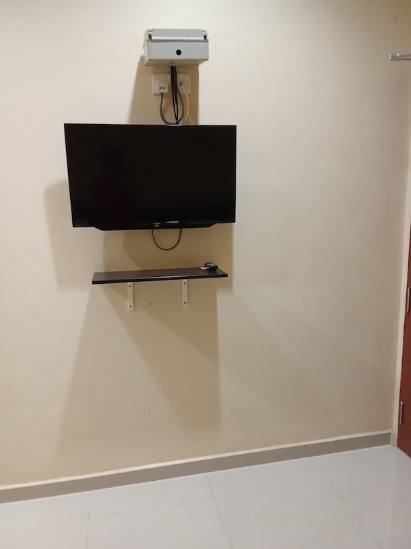 A wall-mounted television with a stand below it, a power outlet above, and a door to the right.