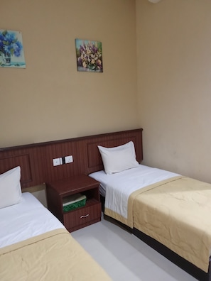 A hotel room with two single beds, a wooden nightstand, a small drawer, and two wall-mounted paintings.