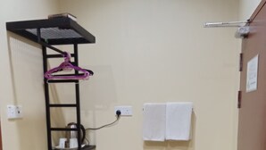 A small bathroom with a black shelf holding toiletries, a green trash bin, and a towel hanging on the wall. - Tanjong Inn by StayZy (Kota Bharu)