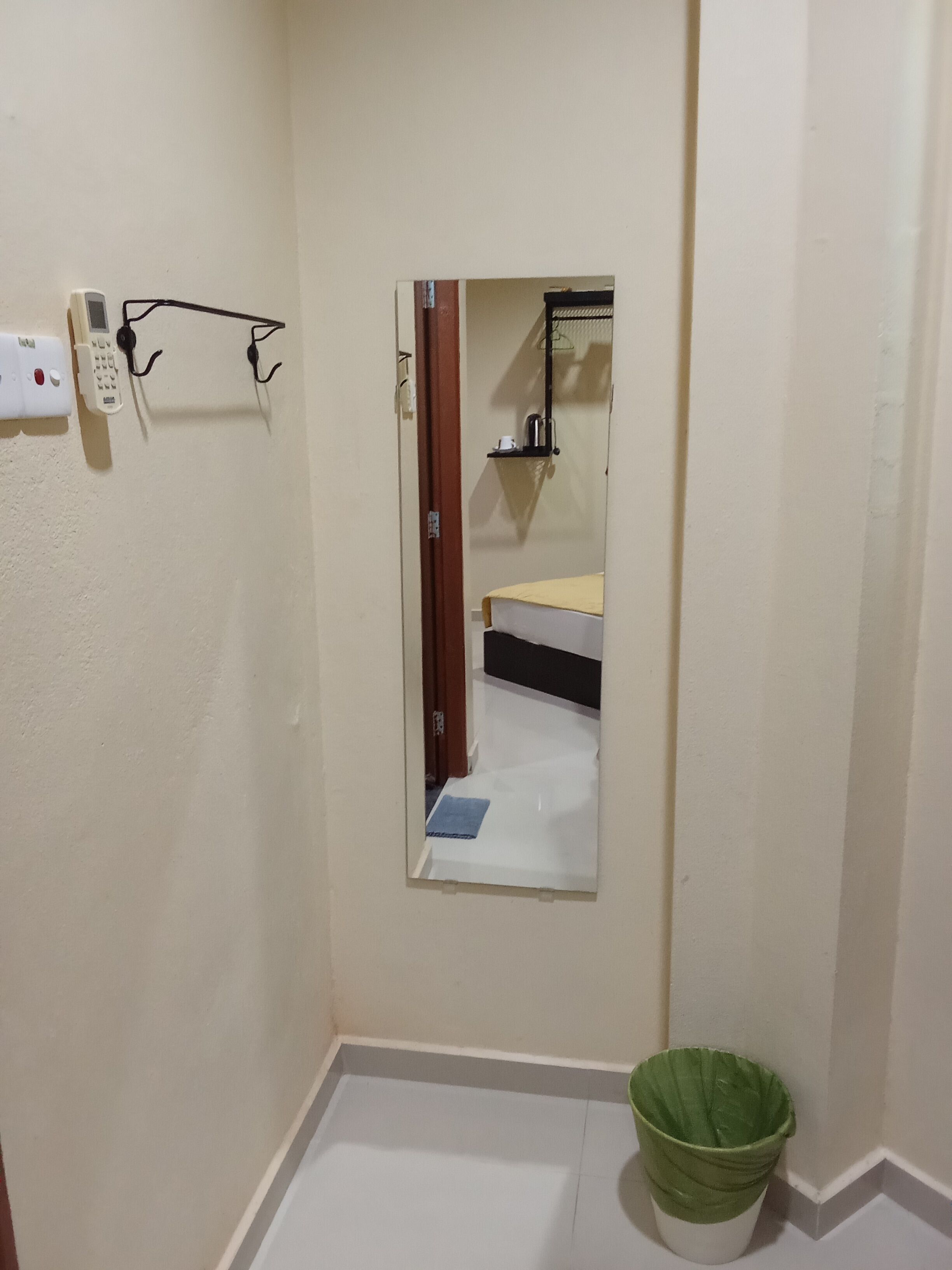 Una habitación pequeña con un espejo, un teléfono y un bote de basura verde.