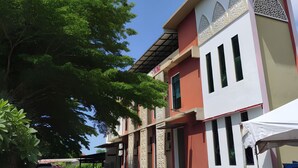 A building with a paved courtyard, a covered area, and a blue car parked outside. - Tanjong Inn by StayZy (Kota Bharu)
