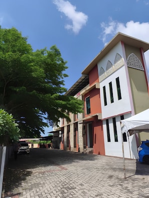 A building with a paved courtyard, a covered area, and a blue car parked outside.