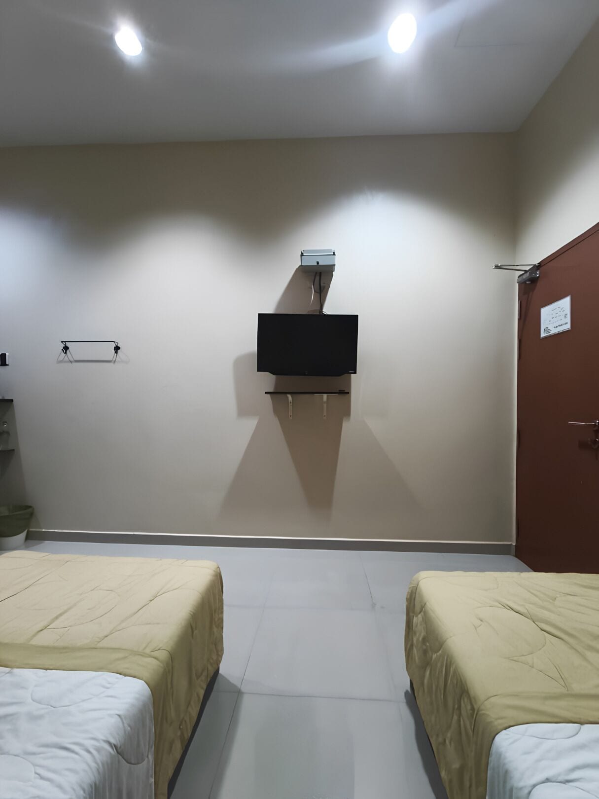 A room with two beds, a television mounted on the wall, and a door on the right.