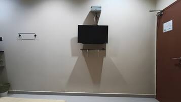 A room with two beds, a television mounted on the wall, and a door on the right.