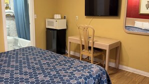 Hotellihuone, jossa on sänky, työpöytä, tuoli, televisio ja kylpyhuone, joka näkyy avoimesta ovesta.