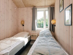 A room with two single beds, a window with curtains, a wall-mounted lamp, and framed pictures. - 4 Star Holiday Home in Vaeggerlose (Vaeggerlose)