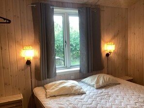 Ein Zimmer mit einem Bett, zwei Wandlampen, einem Fenster mit Vorhängen und einer Bank.