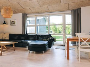 A modern living room with a black leather sofa, wooden coffee table, and a dining table with chairs. - 4 Star Holiday Home in Vaeggerlose (Vaeggerlose)