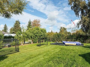 A grassy outdoor area with a trampoline, a fenced play area, and a flagpole. - 4 Star Holiday Home in Vaeggerlose (Vaeggerlose)