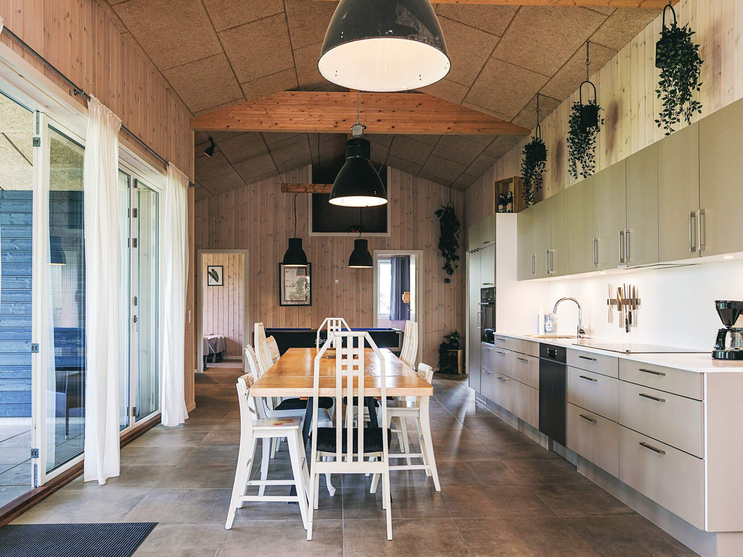 A modern kitchen with wooden walls, a dining area with white chairs, and pendant lighting.