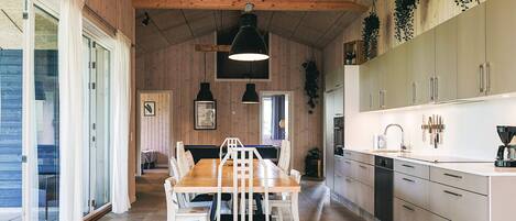 A modern kitchen with wooden walls, a dining area with white chairs, and pendant lighting.