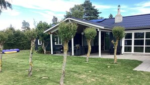 A house with a covered patio, a chimney, and a lawn with young trees. - 4 Star Holiday Home in Vaeggerlose (Vaeggerlose)