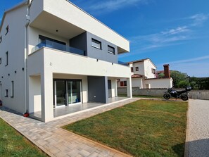 Une maison moderne à deux étages, dotée d’un toit plat, de grandes fenêtres et d’une allée pavée.
