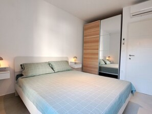 Quarto com cama, mesas de cabeceira, guarda-roupa e ar condicionado.