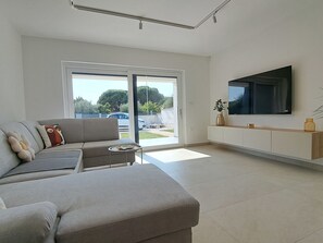 A modern living room with a grey sofa, a small round table, and a TV mounted on the wall. - Vacation home Duplex by Interhome (Pula/Puntižela)