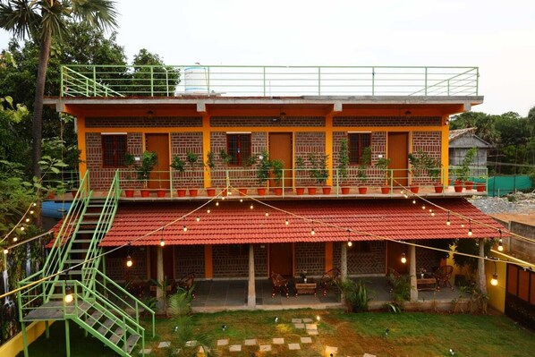 A two-story building with a red-tiled roof, a balcony with potted plants, and a staircase leading to the upper level.