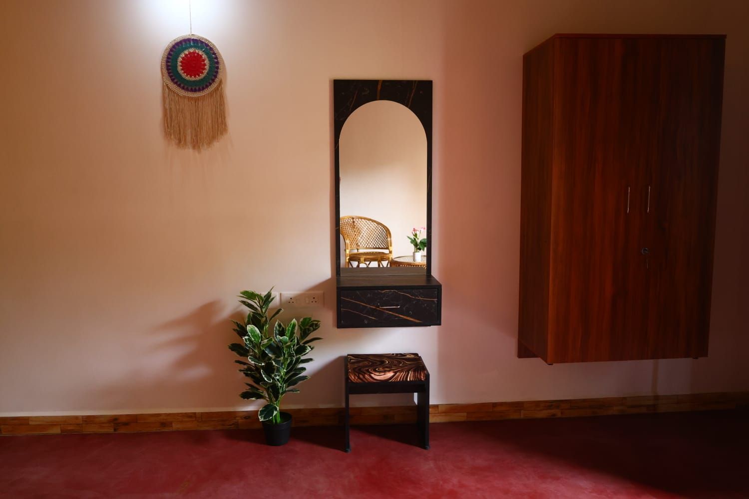 A room with a mirror, a small stool, a potted plant, and a wooden cabinet.