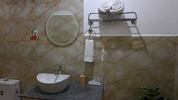 Un baño con pared de mármol, un espejo redondo, un lavabo con grifo, un perchero con toallas y un dispensador de jabón.