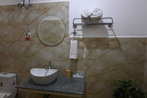 A bathroom with a marble wall, a round mirror, a sink with a faucet, a towel rack with towels, and a soap dispenser.