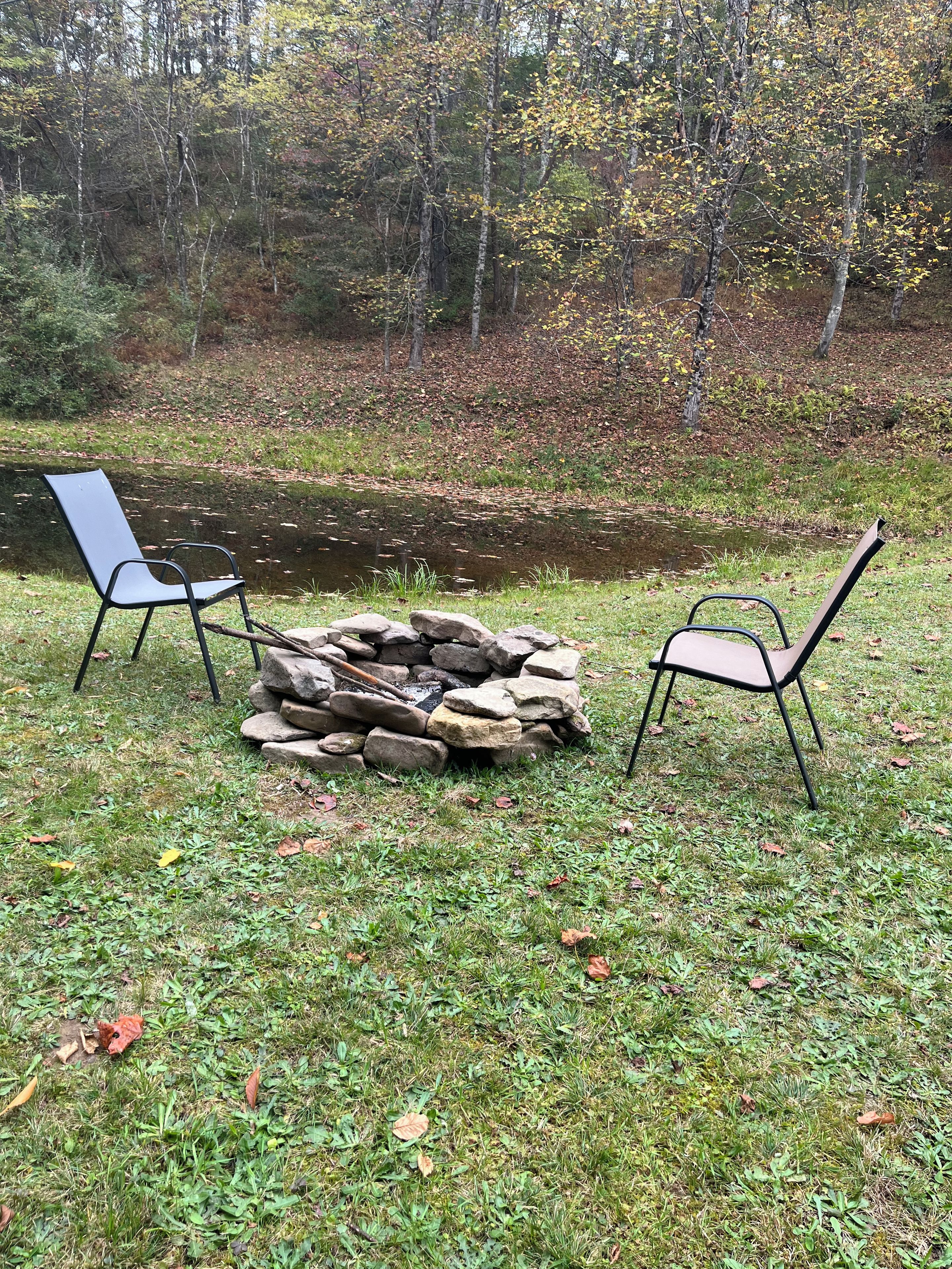 A natural outdoor setting with a stone fire pit and two chairs.
