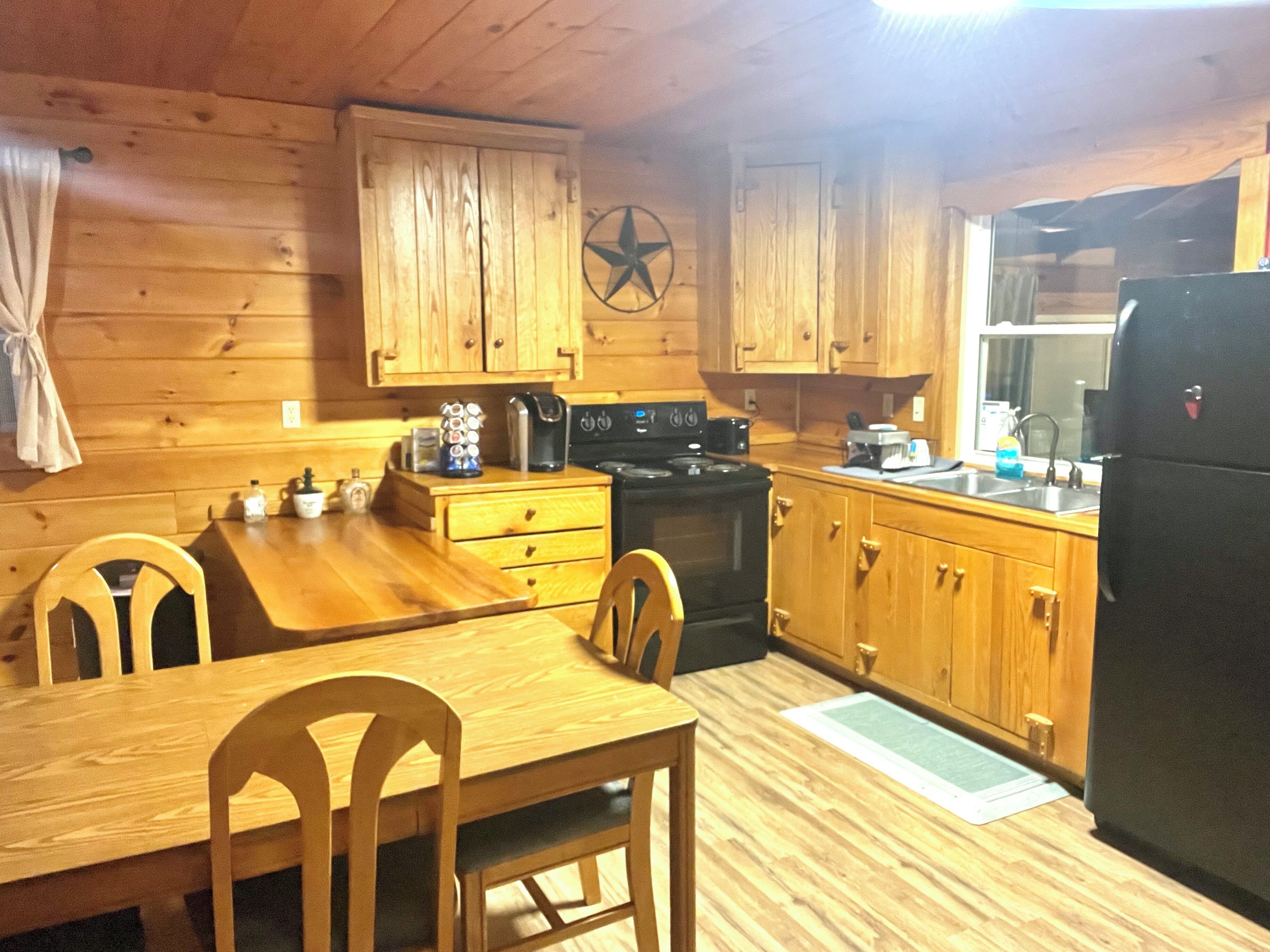 A wooden cabin interior with a dining table, chairs, a stove, and wooden cabinets.