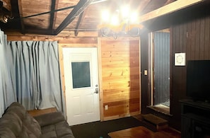 A room with a wooden interior, a white door, a gray sofa, and a television on a wooden stand.