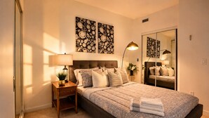 Een slaapkamer met een groot bed, nachtkastje met een lamp, een spiegel en kunst aan de muur.