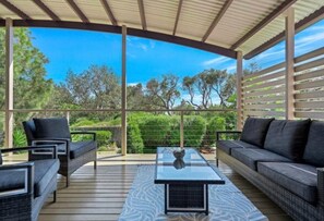 An outdoor patio with wicker furniture, a glass-top table, and a view of trees and sky. - Ultimate Beach Escape: Family Haven, Firepit, near Café, Pets welcome, Sleeps 8 (Culburra Beach)