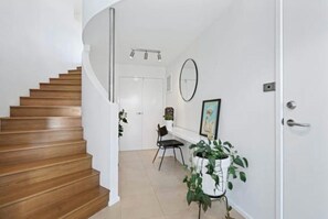 A staircase leading to a room with a white door, a chair, a potted plant, and a framed picture on the wall. - Ultimate Beach Escape: Family Haven, Firepit, near Café, Pets welcome, Sleeps 8 (Culburra Beach)