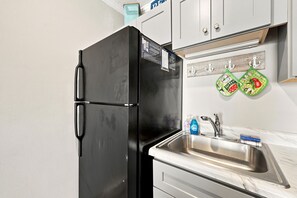 A kitchen with a black refrigerator, a stainless steel sink, and a wooden backsplash. - Water's Edge | Coastal Condo with Ocean Views (North Topsail Beach)