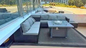 Terraza en la azotea con un sofá modular, una mesita y baranda de vidrio.