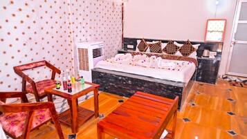 A hotel room with a bed, a desk with a chair, a heater, and a small table with bottles.