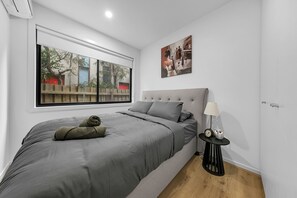 Een slaapkamer met een groot bed, een nachtkastje, een lamp en een schilderij aan de muur.