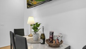 Ein Essbereich mit einem Tisch für zwei Personen, ausgestattet mit einer Lampe, einer Flasche, Gläsern und Snacks.