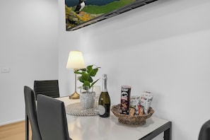 Ein Essbereich mit einem Tisch für zwei Personen, ausgestattet mit einer Lampe, einer Flasche, Gläsern und Snacks.