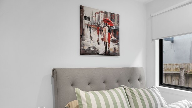 Ein Schlafzimmer mit grauem, gepolsterten Kopfteil, einer Bettdecke in Grün-Weiß-Streifen und einem Gemälde einer Straßenszene über dem Bett.
