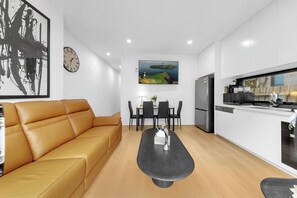 Een moderne woonkamer met een leren bank, een eettafel met stoelen, een keukenhoek met een koelkast, en een klok aan de muur.